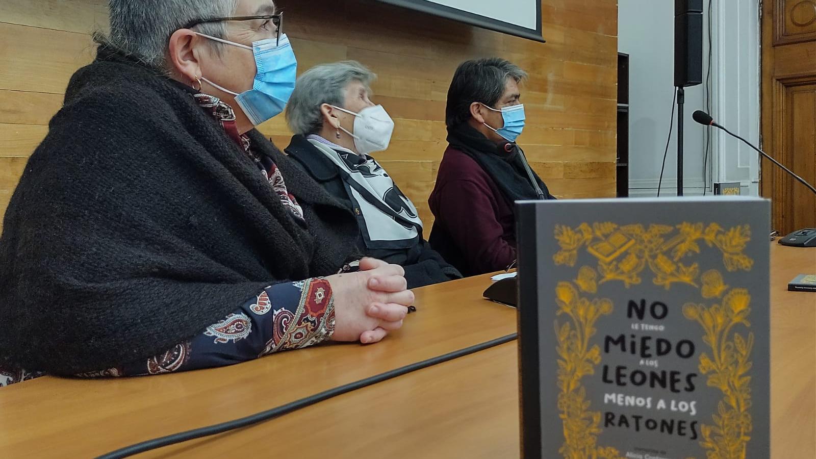 Tres personas en una mesa con micrófonos y en primer plano un libro.