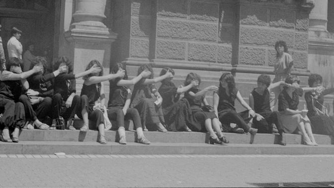 Mujeres protestando sentadas, tapándose sus bocas.